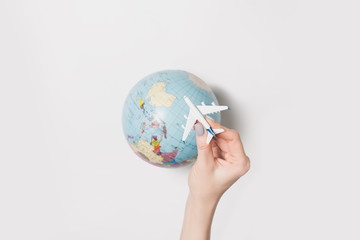 Passenger plane in a female hand on the background of the globe. Flight concept on a light background