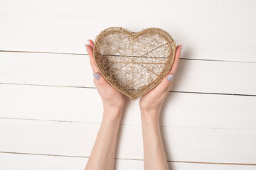 Female hands hold metal wire transparent heart shaped box against the background of a white wooden table