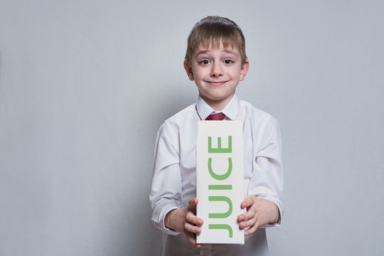 little blond boy holds and shows a big white carton juce package. White shirt and red tie. Light background