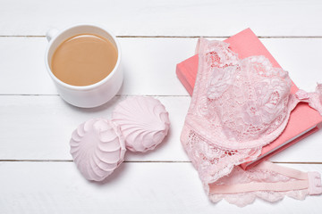 Cup of coffee with marshmallows. Pink lace bodice and notepad on white background. Fashionable concept.
