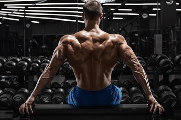 Rear view muscular man showing back muscles at the gym. Strong male naked torso, workout