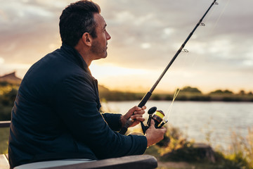 Man sitting near a lake with fishing rod - Powered by Adobe
