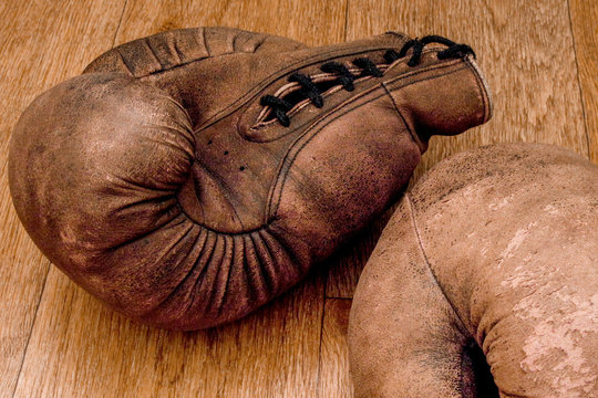 Boxing gloves. Old vintage retro pair of leather worn mittens are on the wood table. Red colors and soft lights. Gloves of retired boxer and fighter