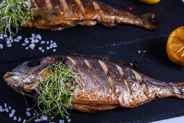 Grilled fish with lemon and spices. Healthy food or diet nutrition concept. Fish Meat on a Black Tray