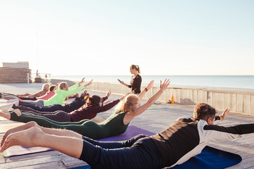 Yoga class at sea beach in evening. Group of people doing yoga poses with yogi instructor on the...