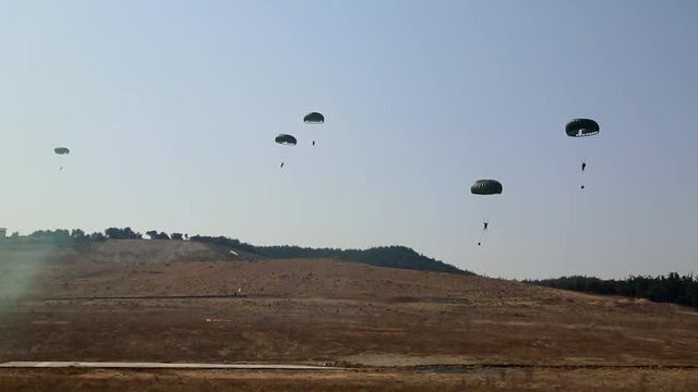 Soldiers landing by parachute in a large open field