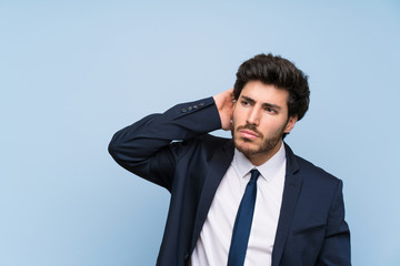 Businessman over isolated blue wall having doubts while scratching head