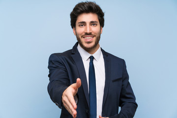 Businessman over isolated blue wall shaking hands for closing a good deal
