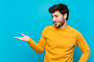 Handsome over isolated blue wall holding copyspace with doubts