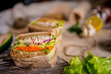 appetizing healthy vegetable sandwich in craft paper on the dark wood table.