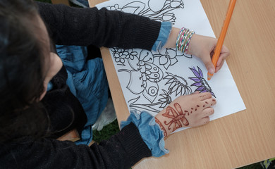 A little girl with Henna tattoo on her hand coloring flowers on paper