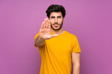 Handsome over isolated purple wall making stop gesture