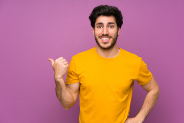 Handsome over isolated purple wall pointing to the side to present a product