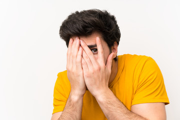 Handsome over isolated white wall covering eyes and looking through fingers