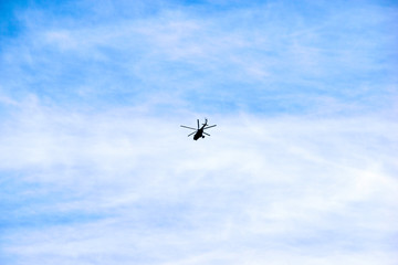 a helicopter flies against the blue sky and clouds