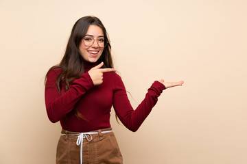 Teenager girl with glasses holding copyspace imaginary on the palm to insert an ad