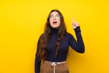 Teenager girl over isolated yellow wall pointing up and surprised