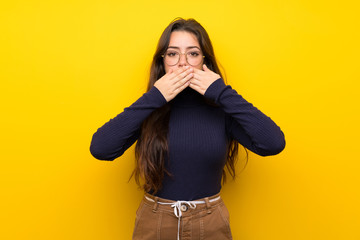 Teenager girl over isolated yellow wall covering mouth with hands