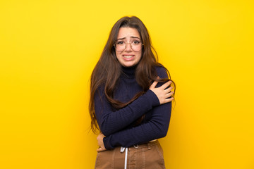 Teenager girl over isolated yellow wall freezing