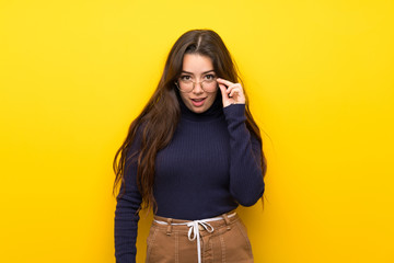 Teenager girl over isolated yellow wall with glasses and surprised