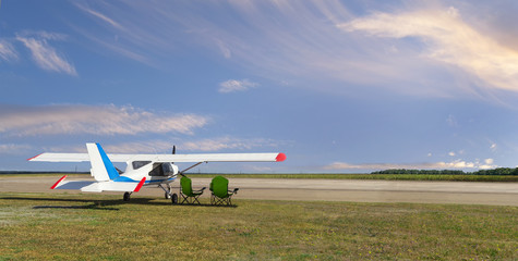 Rear side view of light aircraft with piston engine on airfield with two folding lounge chairs...