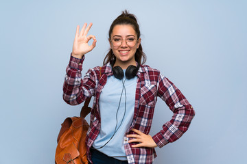Teenager student girl over isolated blue wall showing ok sign with fingers
