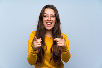 Teenager girl over isolated blue wall points finger at you - obrazy, fototapety, plakaty