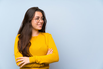Teenager girl over isolated blue wall standing and looking to the side