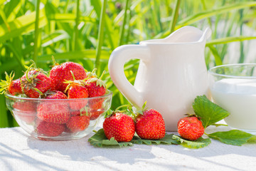 Strawberry berries and leaves, a jug and a cup with milk on a napkin on a background of grass