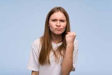 Young woman over blue wall with angry gesture