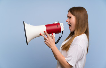 Young woman over blue wall shouting through a megaphone