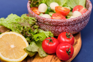 fresh vegetables and a bowl of salad with mozzarella on a blue background.  Caprese salad . Lettuce, cherry tomatoes, mozzarella, 