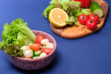 fresh vegetables and a bowl of salad with mozzarella on a blue background.  Caprese salad . Lettuce, cherry tomatoes, mozzarella, 
