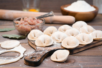 Fototapeta na wymiar Raw dumplings on the cutting board and ingredients for their preparation on a wooden table
