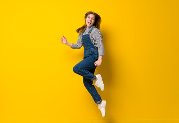 Fototapeta na wymiar Young girl with overalls jumping over isolated yellow background