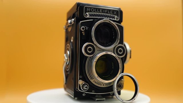 Small rectangular black metalic camera of vintage desigh with lens standing and turning around. Retro style photography of old times