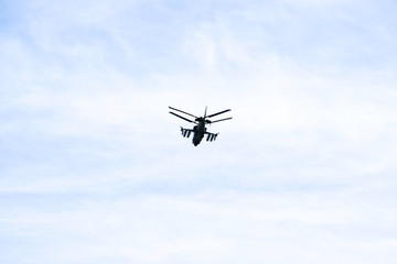 Russian military combat attack helicopter K-52 Alligator flies against a blue sky and clouds