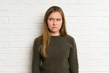 Young woman over white brick wall having doubts and with confuse face expression
