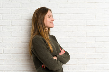Young woman over white brick wall standing and looking to the side