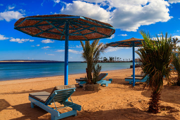 Sun umbrellas and chaise lounges on tropical beach. Concept of rest, relaxation, holidays, resort