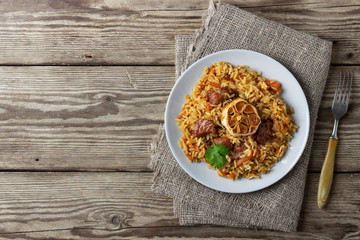 Oriental cuisine. Uzbek pilaf or plov from rice and meat. Wooden rustic background. Top view vith copy space.