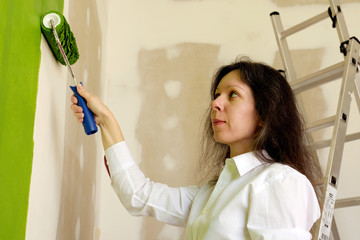 Young woman in white shirt is smiling and painting a wall in green with a roller