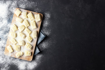 Raw uncooked homemade potato gnocchi with flour on cutting board. Top view. Dark background.