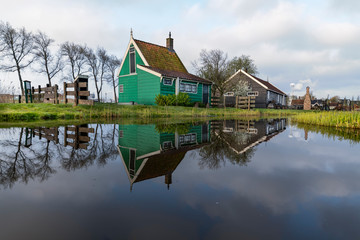 Obraz premium Long exposure of a reflection of the wooden green houses topped with dark orange color roof reflected on the calm water of the canal