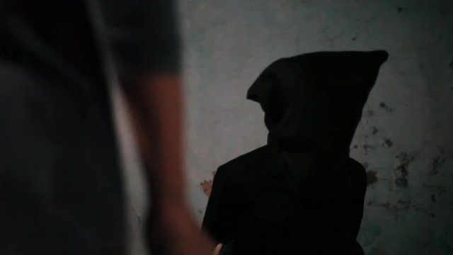 Dolly shot of a man wearing green colored t-shirt and moving towards the other man which is wearing black colored attire with a bag covering his face.