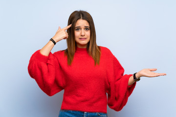 Young woman over isolated blue wall making the gesture of madness putting finger on the head