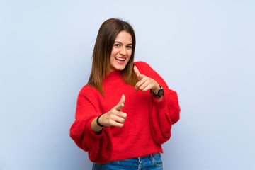 Young woman over isolated blue wall pointing to the front and smiling