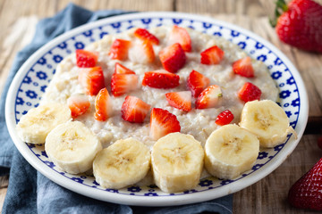 Oatmeal Porridge with Strawberries and banana on wooden rustic table. Healthy Breakfast with Fresh Organic Berries.