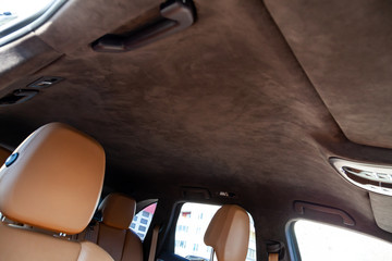 The ceiling of the SUV car pulled by brown soft material alkantara in the workshop for tuning and styling the interior, view from the passanger opened door on central mirror and sun visorson the roof