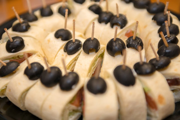 Meat rolls in pita bread with black olives on a plate.